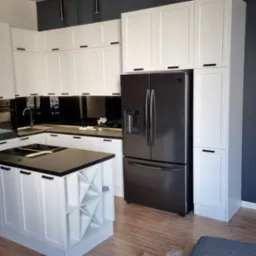 Nowoczesna, biała kuchnia z czarnymi akcentami: wyspa z półkami na wino, zabudowana lodówka, czarny backsplash i ciemna ściana.