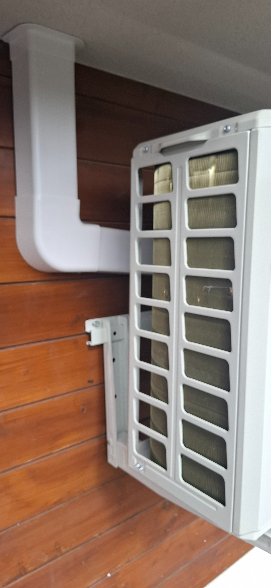 Biała jednostka wewnętrzna klimatyzacji zamontowana na drewnianej ścianie, widoczne rury instalacyjne. Kątowe ujęcie detalu.