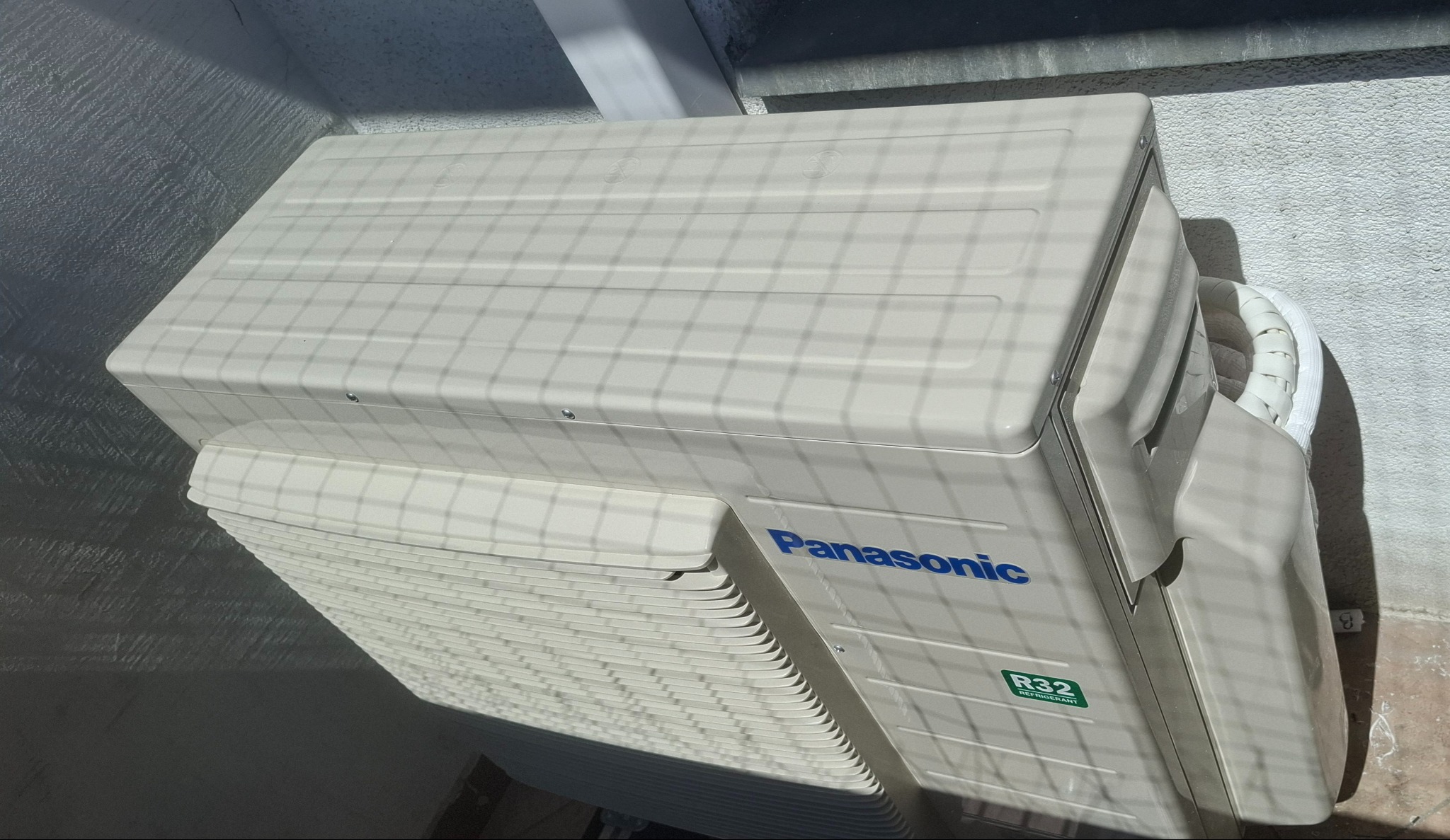 Zewnętrzna jednostka klimatyzacji Panasonic R32 zamontowana przy ścianie budynku, widoczna z góry pod kątem, oświetlona promieniami słonecznymi.