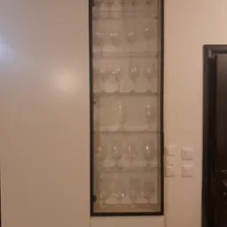 Biała szafa na wymiar z przeszkloną witryną, prezentująca kolekcję kieliszk&oacute;w w Elblągu. Minimalistyczny design, proste linie, czarna rama witryny.