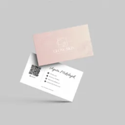 Dwie wizytówki na szarym tle, jedna z logo i grafiką kwiatową w odcieniach różu, druga z danymi kontaktowymi i kodem QR dla gabinetu kosmetycznego Glow Skin.