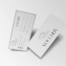 Dwa minimalistyczne vouchery na usługi salonu urody, z logo i danymi kontaktowymi, leżące na białym tle.