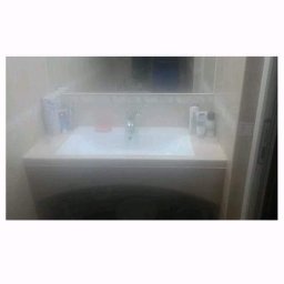 RemBudserwis - Umywalka w zabudowie z białym blatem, lustro w tle, akcesoria łazienkowe na blacie, widok z dołu.