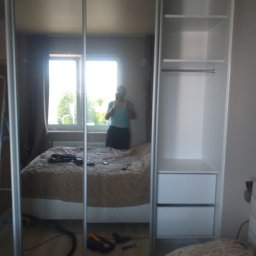 RemBudserwis - Biała szafa wnękowa z lustrzanymi drzwiami przesuwnymi i otwartymi półkami, widoczna w odbiciu sypialnia z oknem i osoba robiąca zdjęcie.