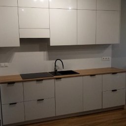 RemBudserwis - Biała, nowoczesna kuchnia z drewnianym blatem i czarną armaturą, oświetlona punktowymi lampami, prezentująca minimalistyczny design.