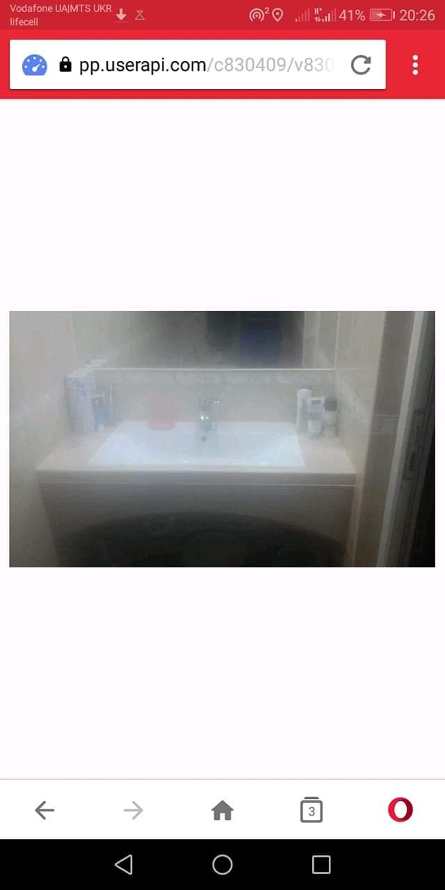 Umywalka w zabudowie z białym blatem, lustro w tle, akcesoria łazienkowe na blacie, widok z dołu.