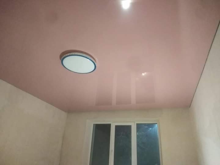 Błyszczący, różowy sufit napinany z zamontowanym okrągłym oświetleniem LED w pokoju z surowymi ścianami i oknem.