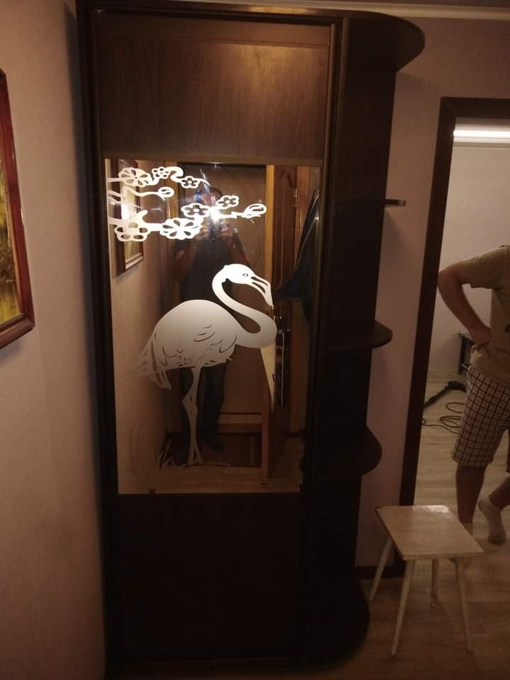 Ciemna szafa wnękowa z lustrem ozdobionym motywem flaminga i kwiatów, widoczna w przedpokoju z elementami garderoby i stołkiem.