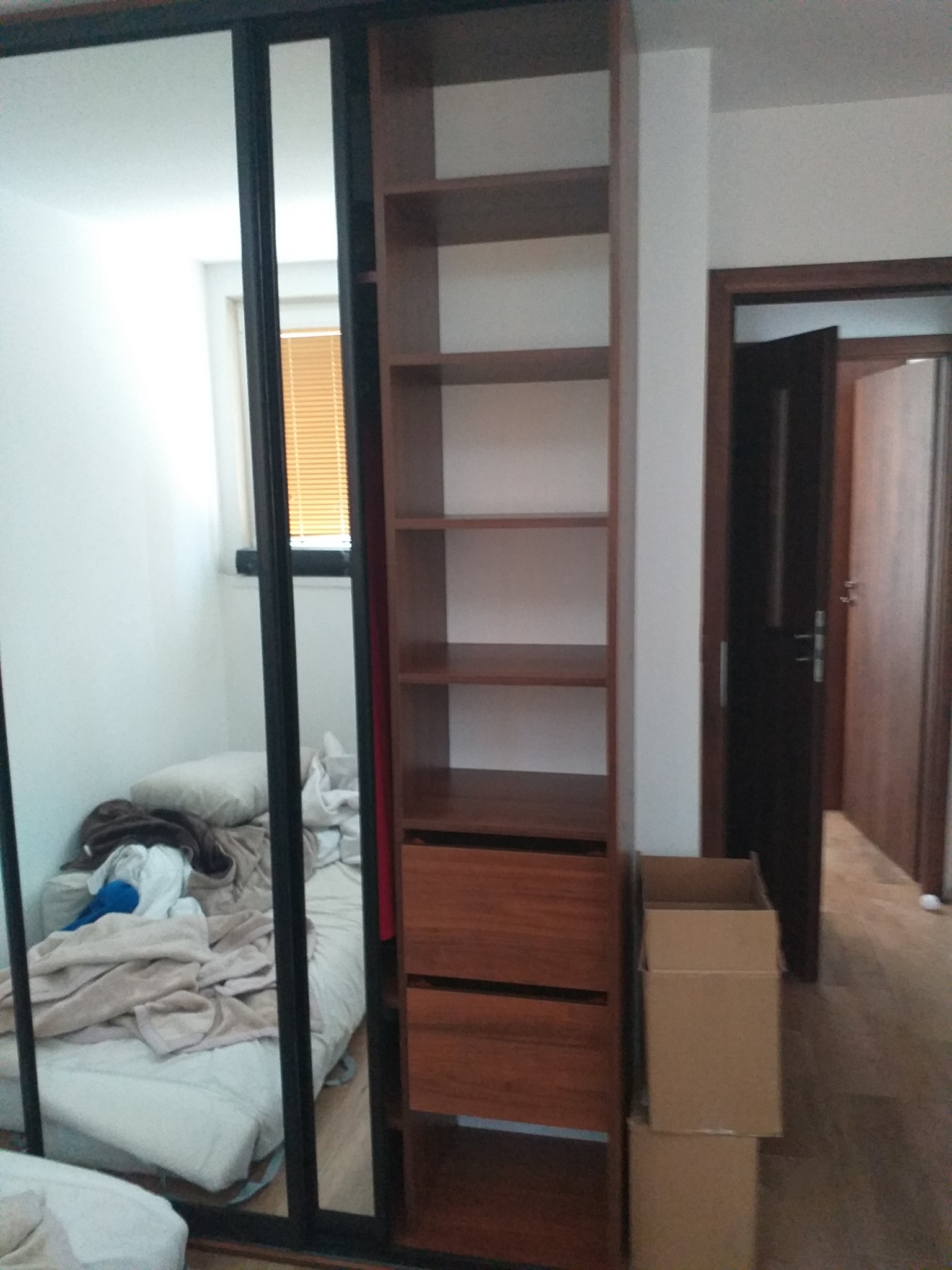 Montaż szafy wnękowej z lustrzanymi drzwiami przesuwnymi i drewnianym regałem, widoczne kartony po montażu.