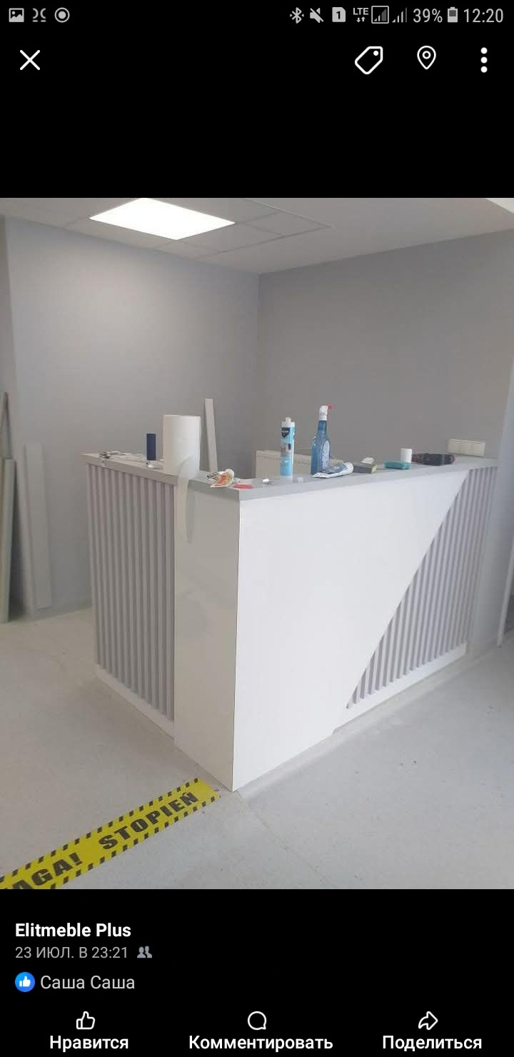 Nowoczesna, biała lada recepcyjna z pionowymi panelami i ukośnym wzorem, w minimalistycznym wnętrzu. Widoczne akcesoria montażowe i taśma ostrzegawcza.