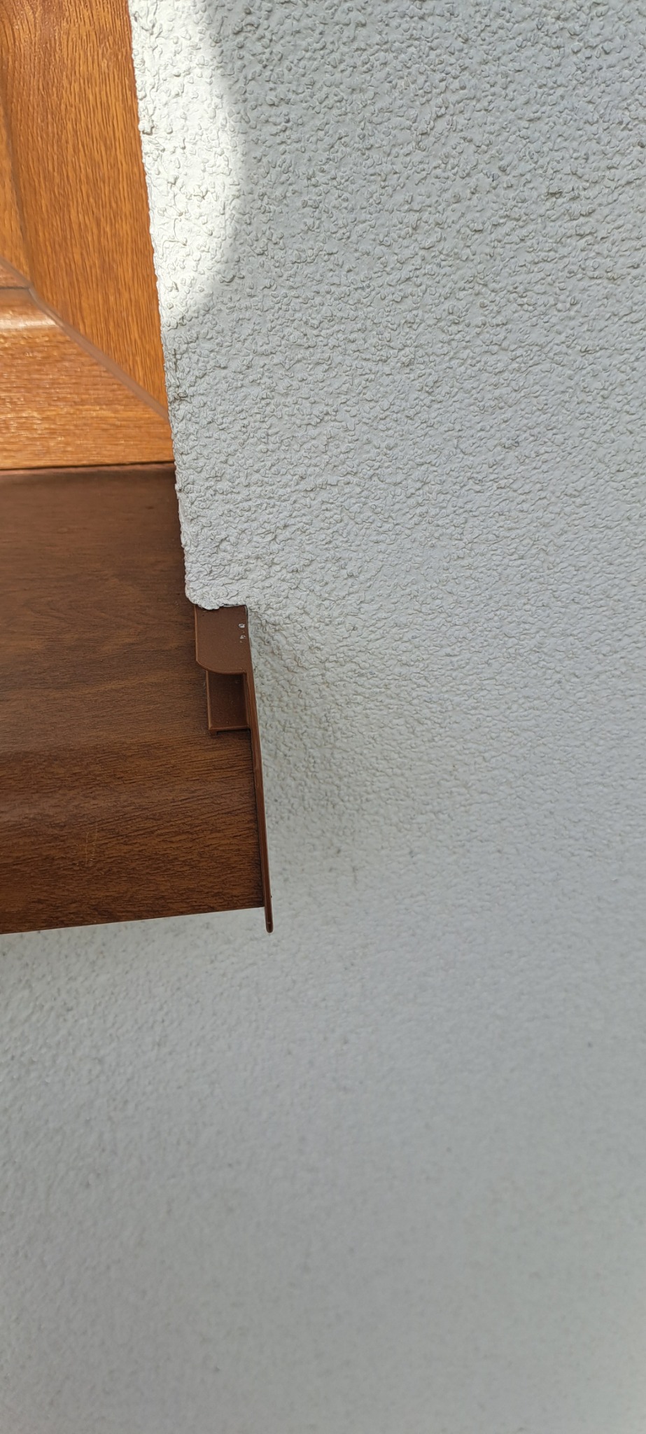 Fragment elewacji z dekoracyjnym, brązowym elementem wykończeniowym pod okapem, widoczna faktura tynku baranka.