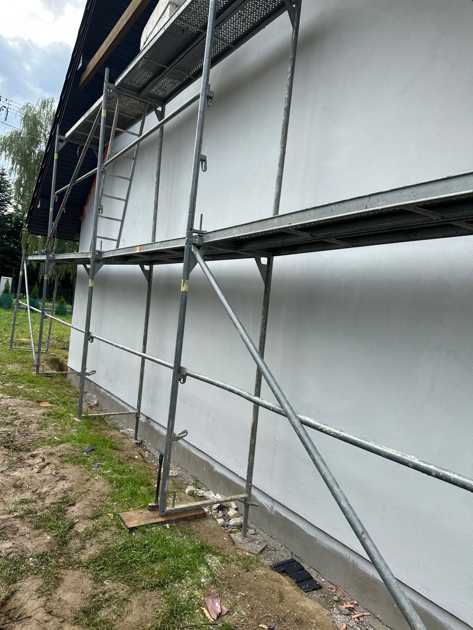 Ściana budynku w trakcie ocieplania, widoczne rusztowanie i świeży tynk.