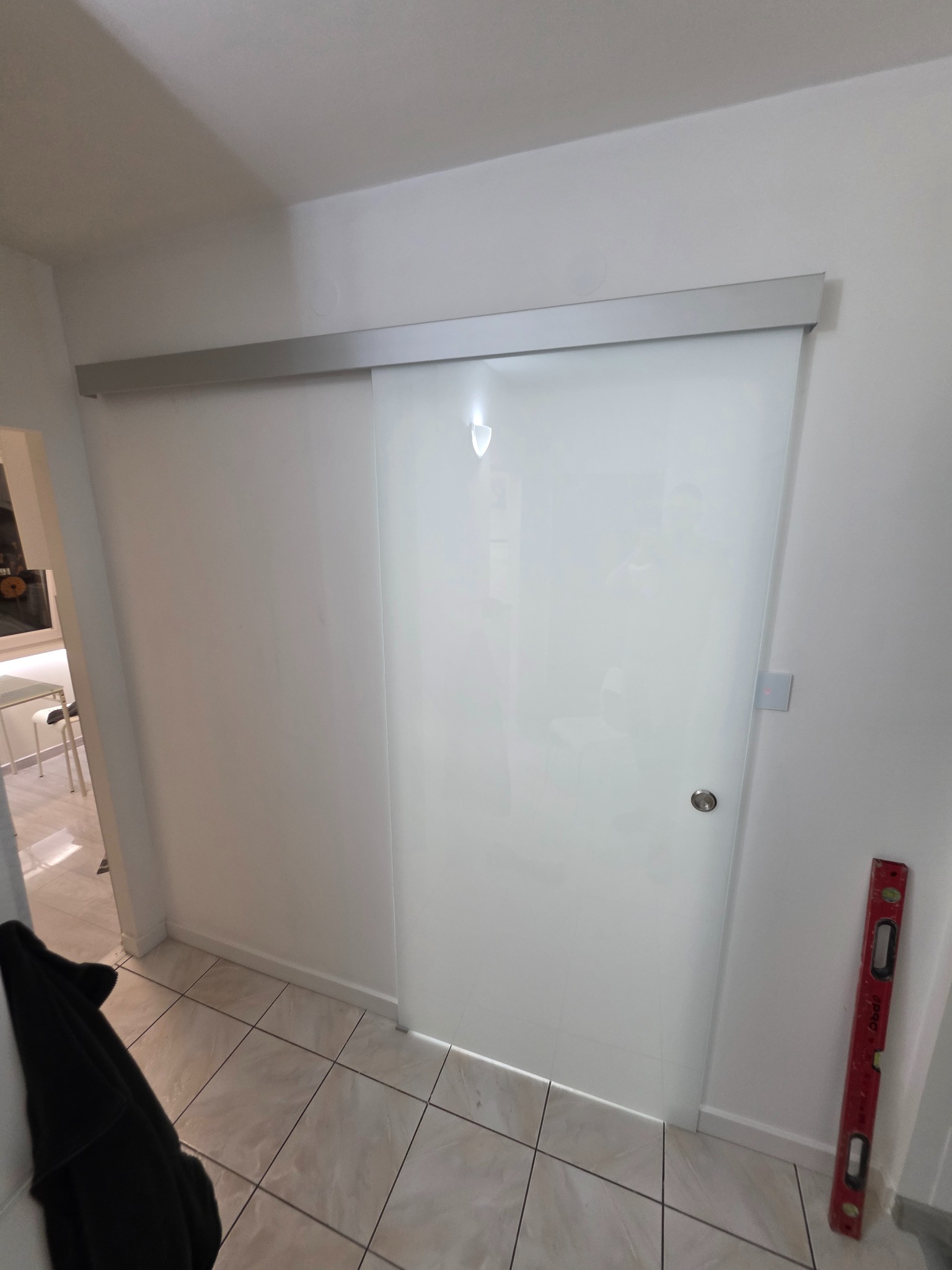 Nowoczesne, przesuwne drzwi szklane z aluminiową prowadnicą w jasnym wnętrzu. Po prawej stronie widoczna poziomica, sugerująca precyzyjny montaż.