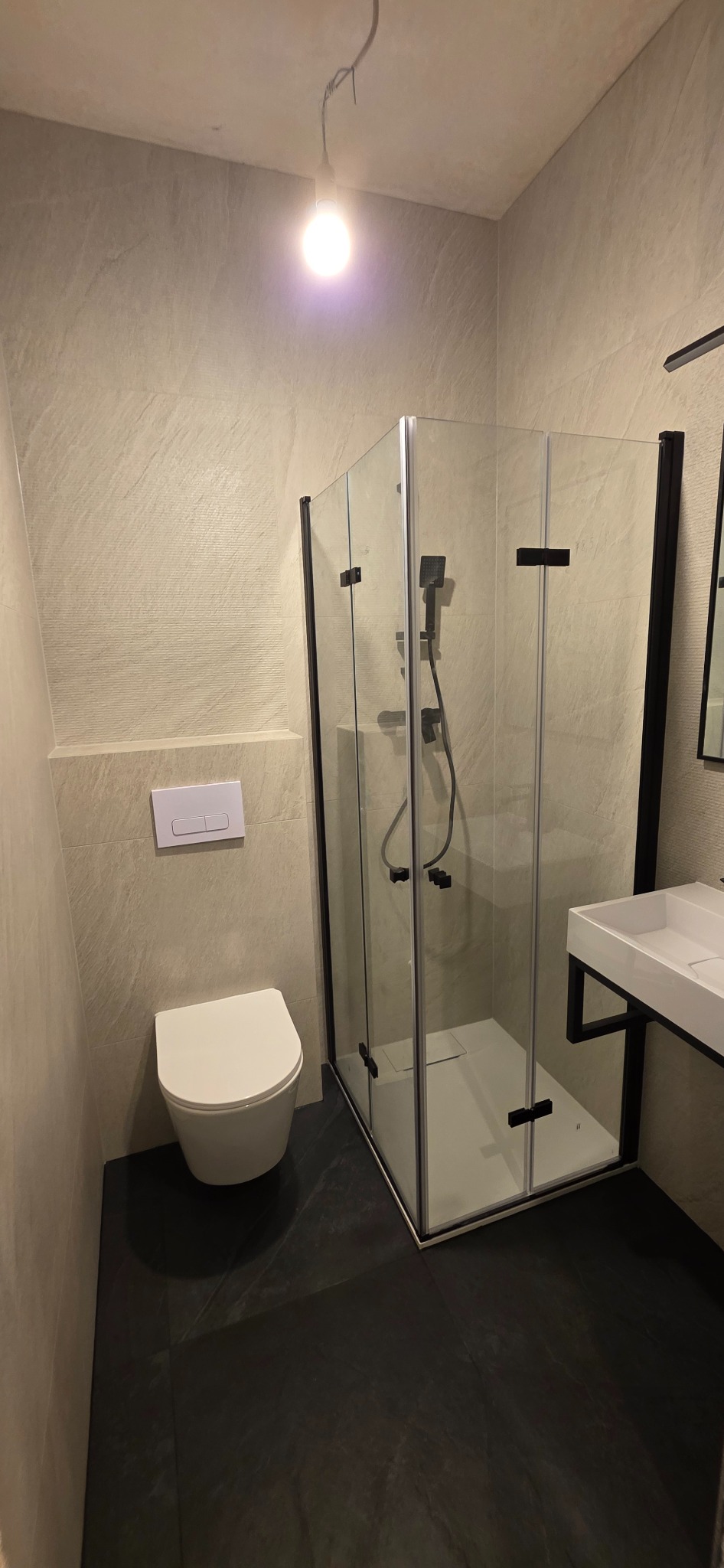 Nowoczesna łazienka w Sidzinie z kabiną prysznicową typu walk-in, wiszącą toaletą i umywalką na czarnym stelażu. Ściany wykończone płytkami imitującymi kamień.