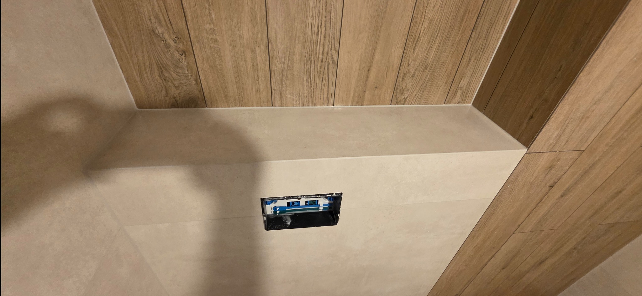 Wykończona wnęka z płytkami imitującymi drewno i beżowymi płytkami. Widoczna puszka elektryczna. Ujęcie z dołu, podkreślające detale wykończenia.