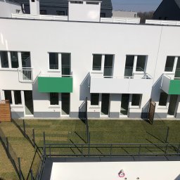 ECOOGRÓD TOMASZ DAROCH - Nowoczesny budynek z balkonami, widok z góry na trawnik z siatką ogrodzeniową, świeżo założony trawnik z rolki z widocznymi łączeniami.