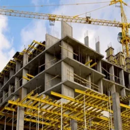 Wznoszenie wielopiętrowego budynku w technologii monolitycznej z widocznym żurawiem wieżowym i szalunkami stropowymi.