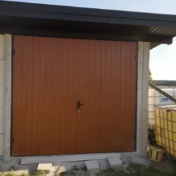 Zamknięta, brązowa brama garażowa z pionowymi panelami, zamontowana w surowej betonowej ramie, z widocznymi zbiornikami na wodę w tle.