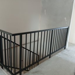 HUB-MAR Marek Piasecki - Nowoczesna, czarna balustrada metalowa na schodach w surowym wnętrzu. Minimalistyczny design, proste linie. Widok z góry na fragment schodów i balustrady.