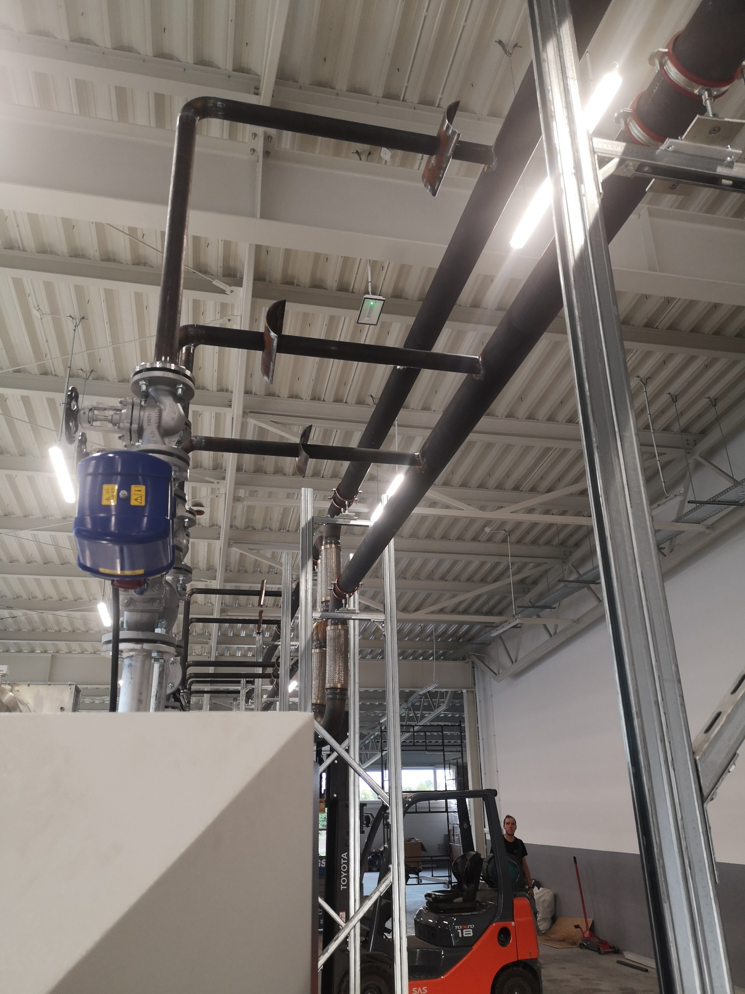 Instalacja rur przemysłowych w hali w Sędziejowicach, widoczny wózek widłowy i pracownik.