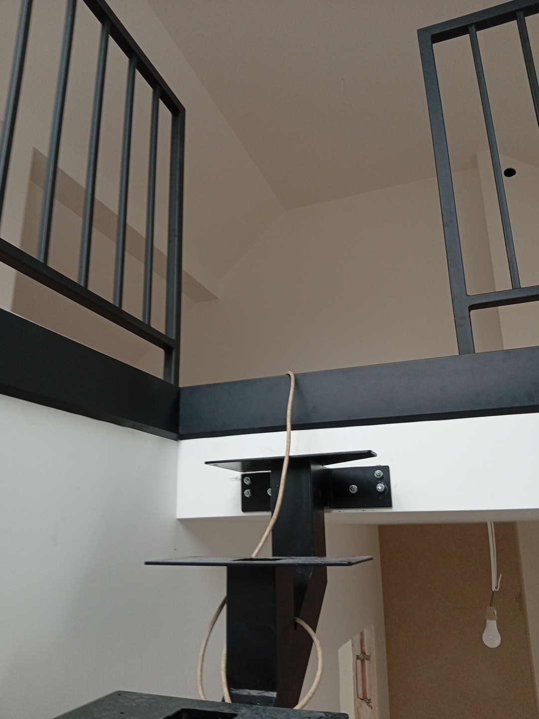 Nowoczesna, czarna balustrada metalowa z pionowymi szczeblami, zamocowana do białej ściany. Widoczne elementy mocujące i fragment konstrukcji nośnej.