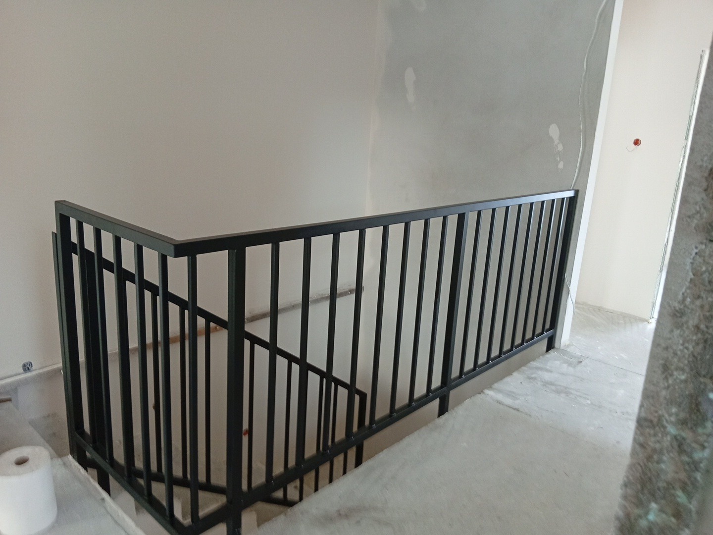 Nowoczesna, czarna balustrada metalowa na schodach w surowym wnętrzu. Minimalistyczny design, proste linie. Widok z góry na fragment schodów i balustrady.