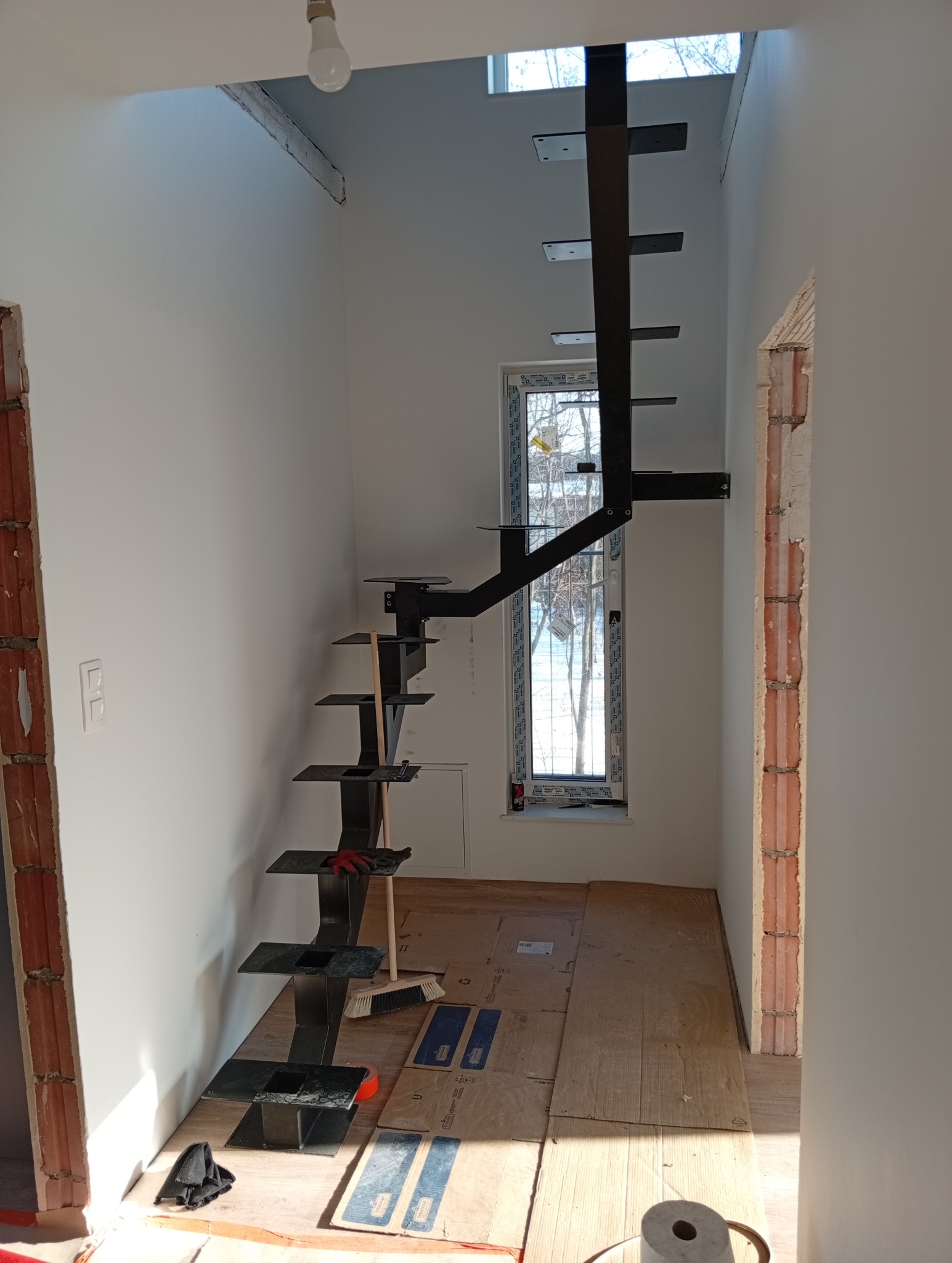 Nowoczesne, czarne schody metalowe wspornikowe w jasnym wnętrzu domu w Sędziejowicach. Widoczne elementy montażowe i zabezpieczenie podłogi kartonem.