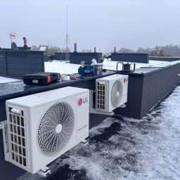 Air Klimat - Dwa białe klimatyzatory LG zamontowane na dachu budynku pokrytym śniegiem. Widoczne narzędzia i sprzęt instalacyjny. W tle budynki i pochmurne niebo.