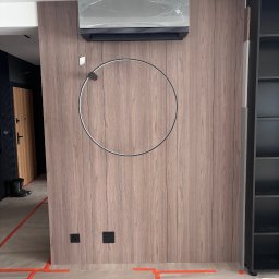 Air Klimat - Zamontowany klimatyzator na drewnianej ścianie z okrągłą lampą. Widoczne zabezpieczenia podłogi taśmą malarską. Nowoczesny design wnętrza.