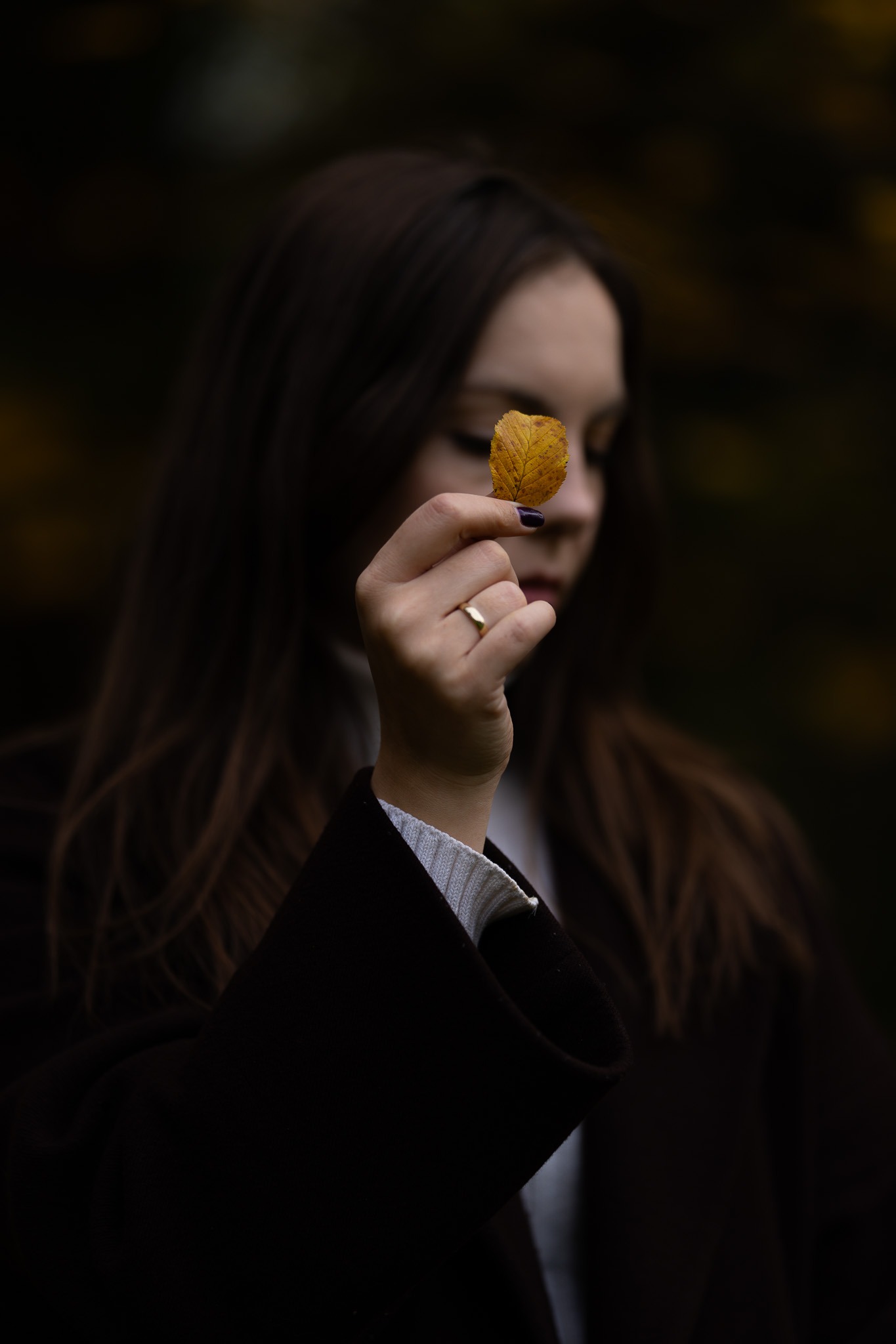 Kobieta z rozmazanym tłem trzyma w dłoni z pierścionkiem na palcu mały, żółty liść na wyciągniętej dłoni.