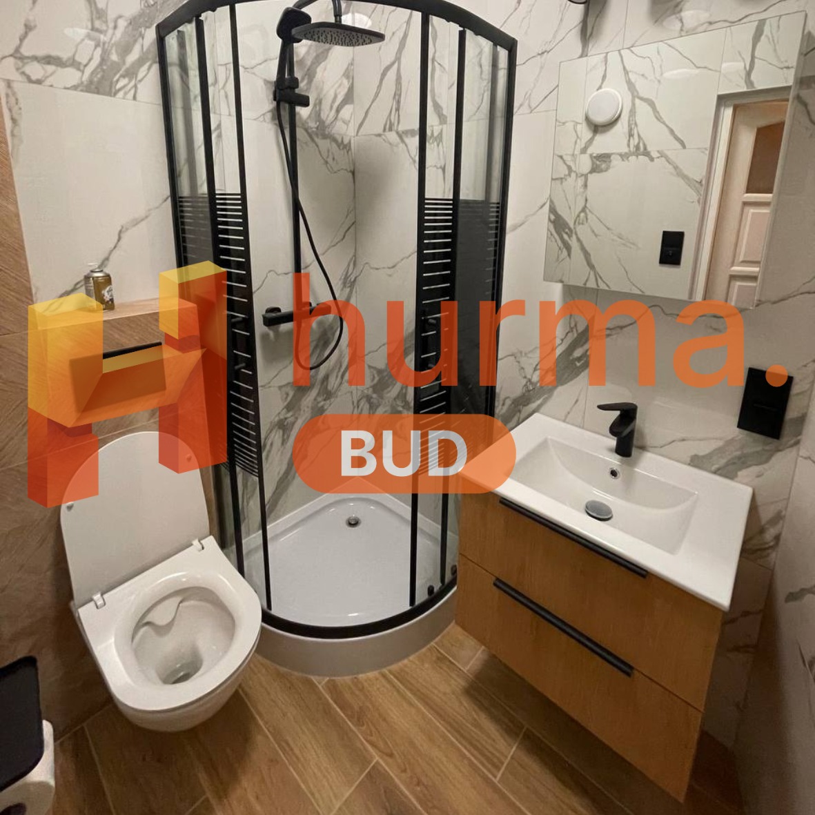 Nowoczesna łazienka po remoncie: kabina prysznicowa z czarnymi profilami, umywalka z szafką w kolorze drewna i biała toaleta, całość wykończona płytkami imitującymi marmur i drewno.