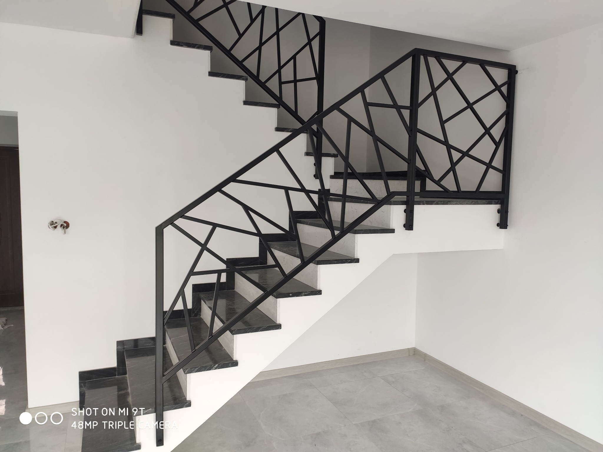 Schody wewnętrzne z czarnymi stopniami z kamienia i nowoczesną, geometryczną balustradą ze stali malowanej na czarno na tle białych ścian.