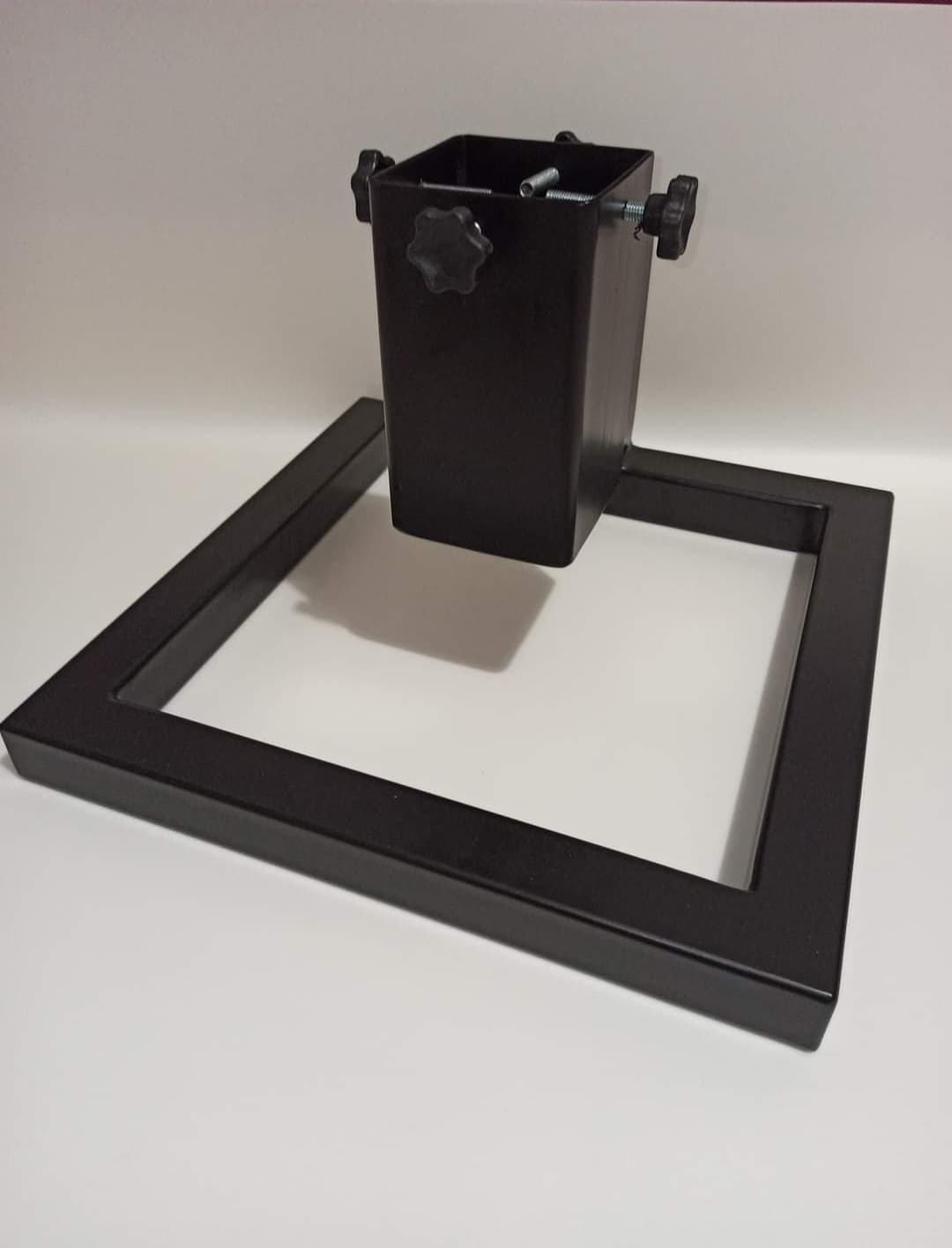 Czarny metalowy stojak na choinkę z regulowanymi śrubami, widoczne sprężyny, na białym tle.