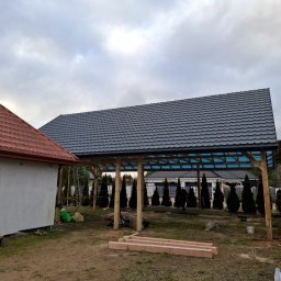 Czar-Bud - Zadaszenie tarasu z ciemnoszarą dachówką, widoczne drewniane słupy konstrukcyjne i fragment dachu budynku z czerwoną dachówką. Tło: pochmurne niebo.