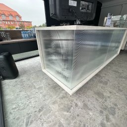 BartServices Bartłomiej Leśniak - Nowoczesna zabudowa meblowa z ryflowanego szkła, widok z dołu, widoczny fragment budynku z czerwonej cegły za oknem.