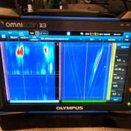 Ekran urządzenia Olympus OmniScan X3 prezentujący wyniki badania ultradźwiękowego, z widocznymi wykresami i danymi pomiarowymi, prawdopodobnie używanego do kontroli jakości spoin spawalniczych.