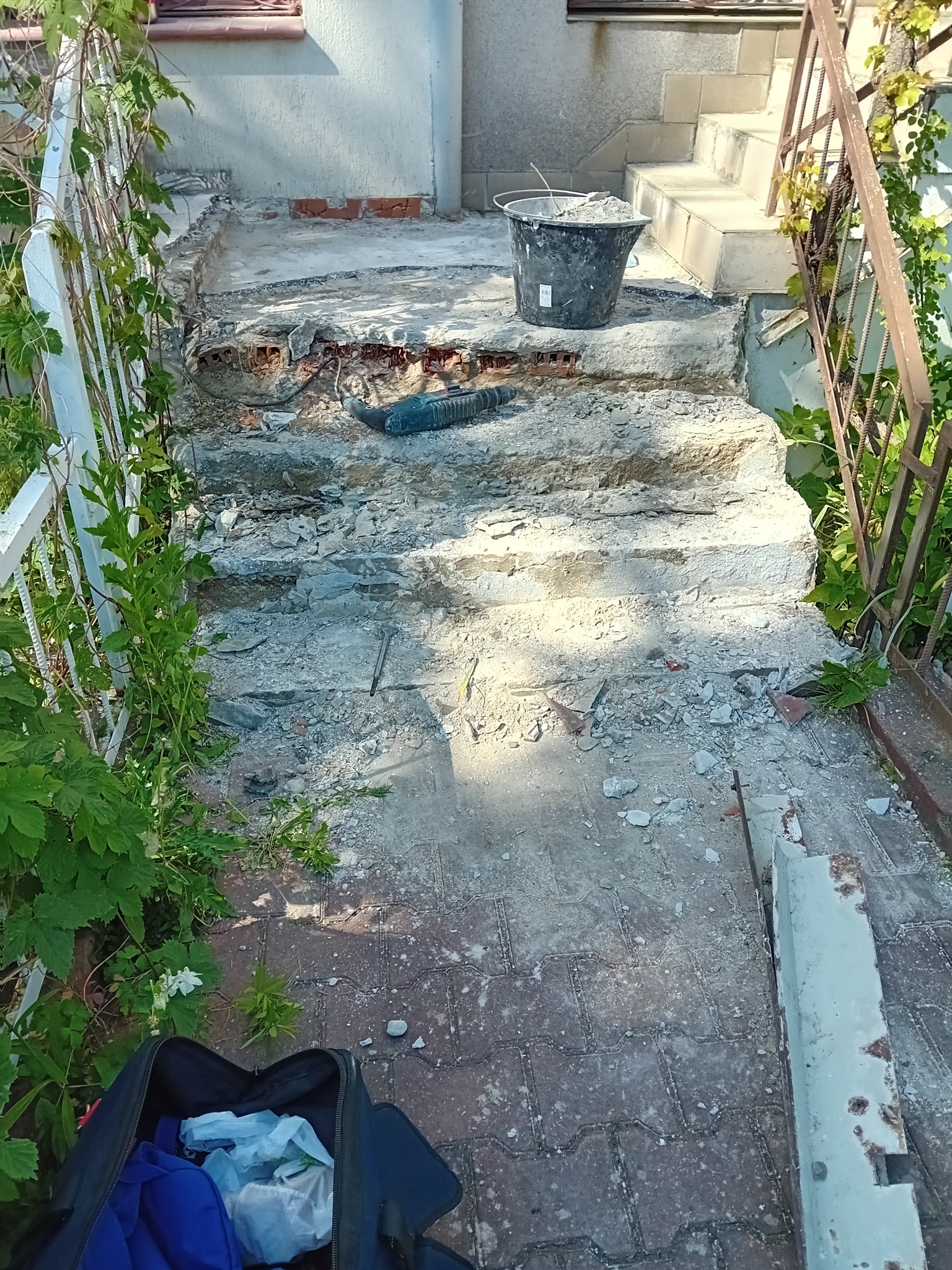 Schody wejściowe w trakcie demontażu starej okładziny, widoczne gruz, wiadro z odpadami i elektronarzędzie