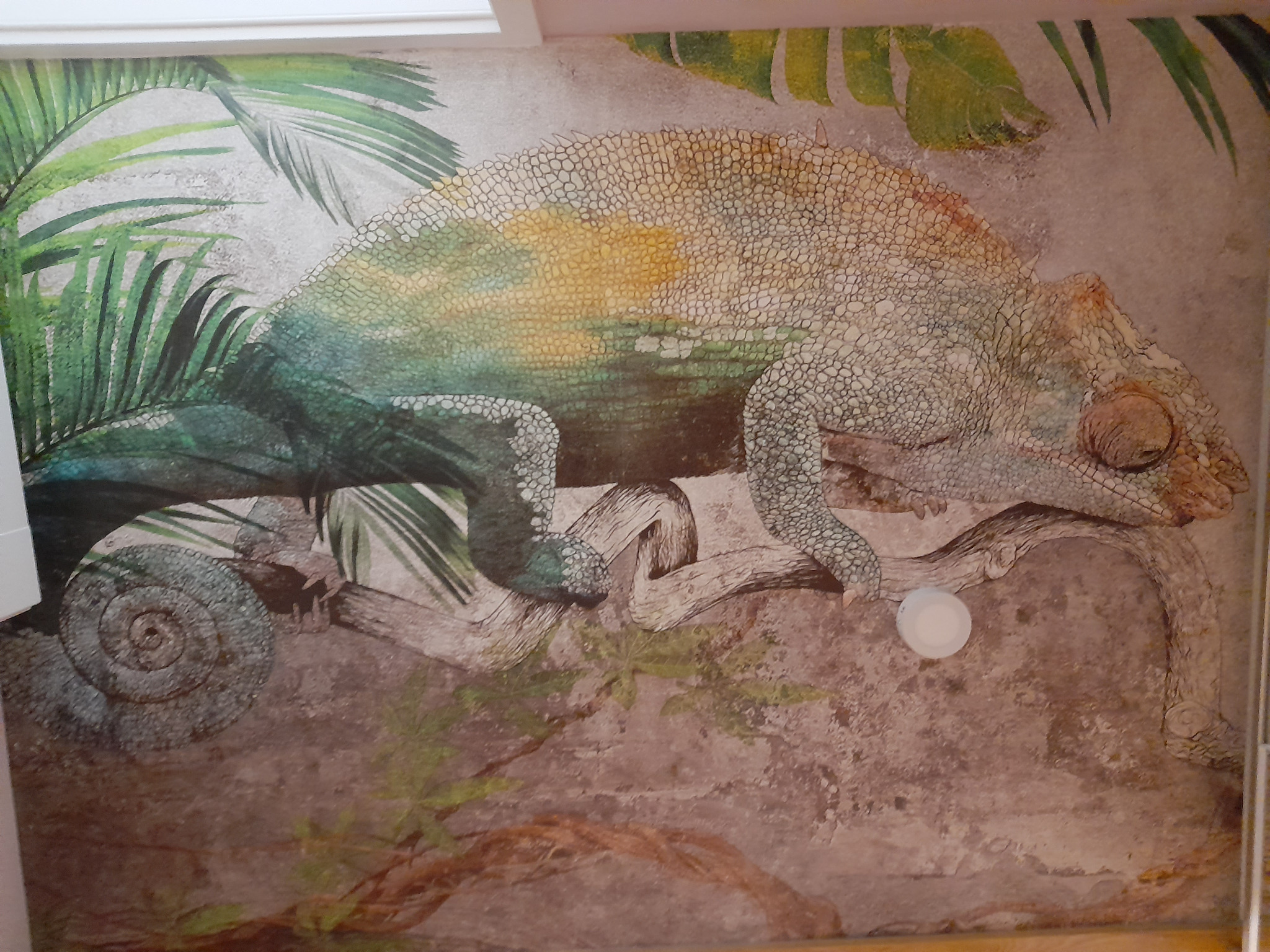 Malowidło ścienne przedstawiające kameleona w tropikalnym otoczeniu, z widocznymi śladami pędzla i teksturą imitującą naturalny kamień.