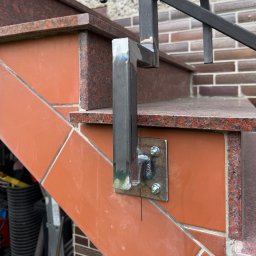 Yurii Ospishchev - Perfect Welding - Spawana konstrukcja metalowa, mocowana do schodów z terakoty i granitu. Widoczne spawy i śruby mocujące. Element balustrady w trakcie montażu.