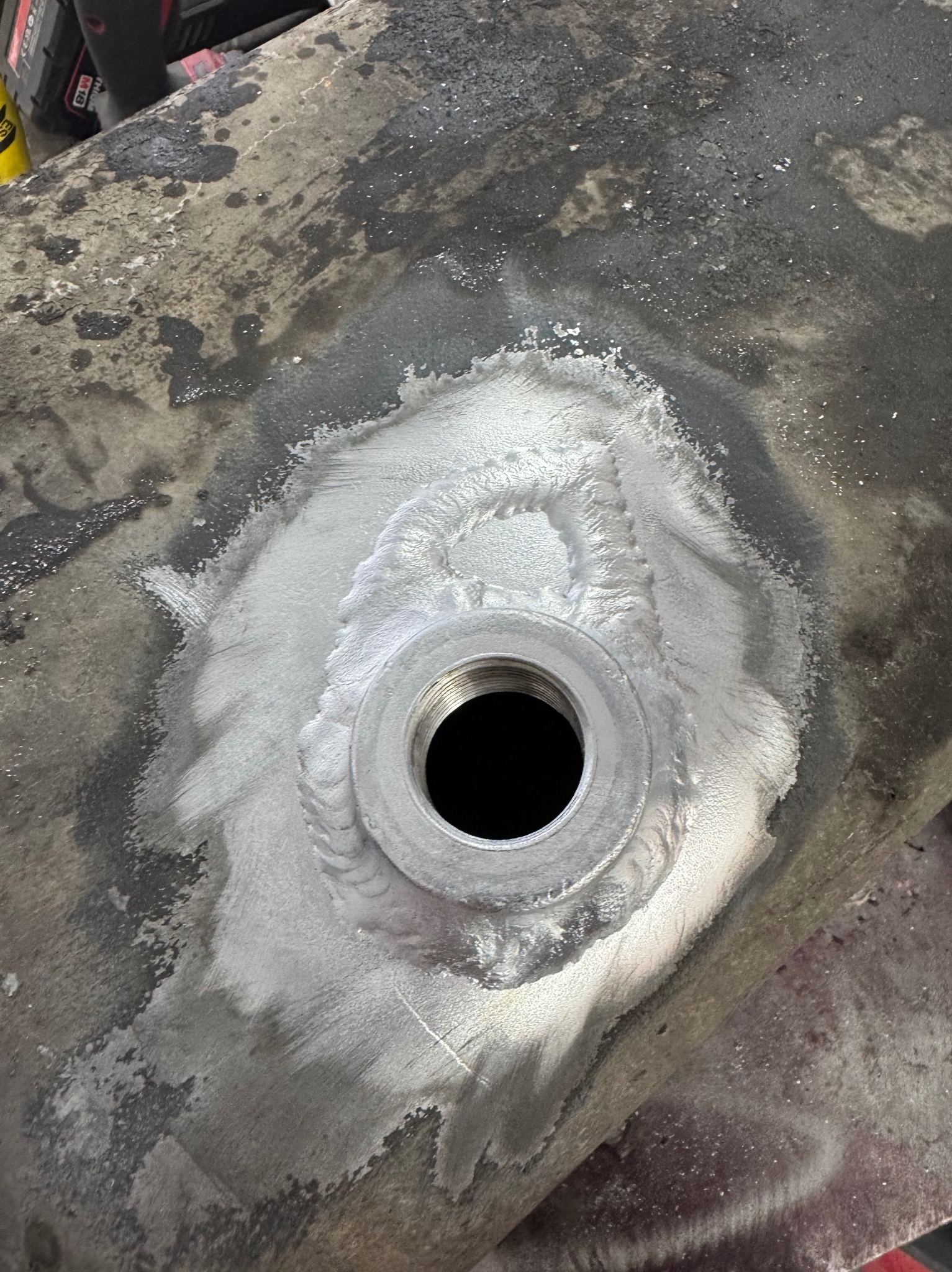 Metalowa powierzchnia z przyspawanym gwintem, widoczne ślady obróbki i spawania. Szlifowana powierzchnia wokół elementu.