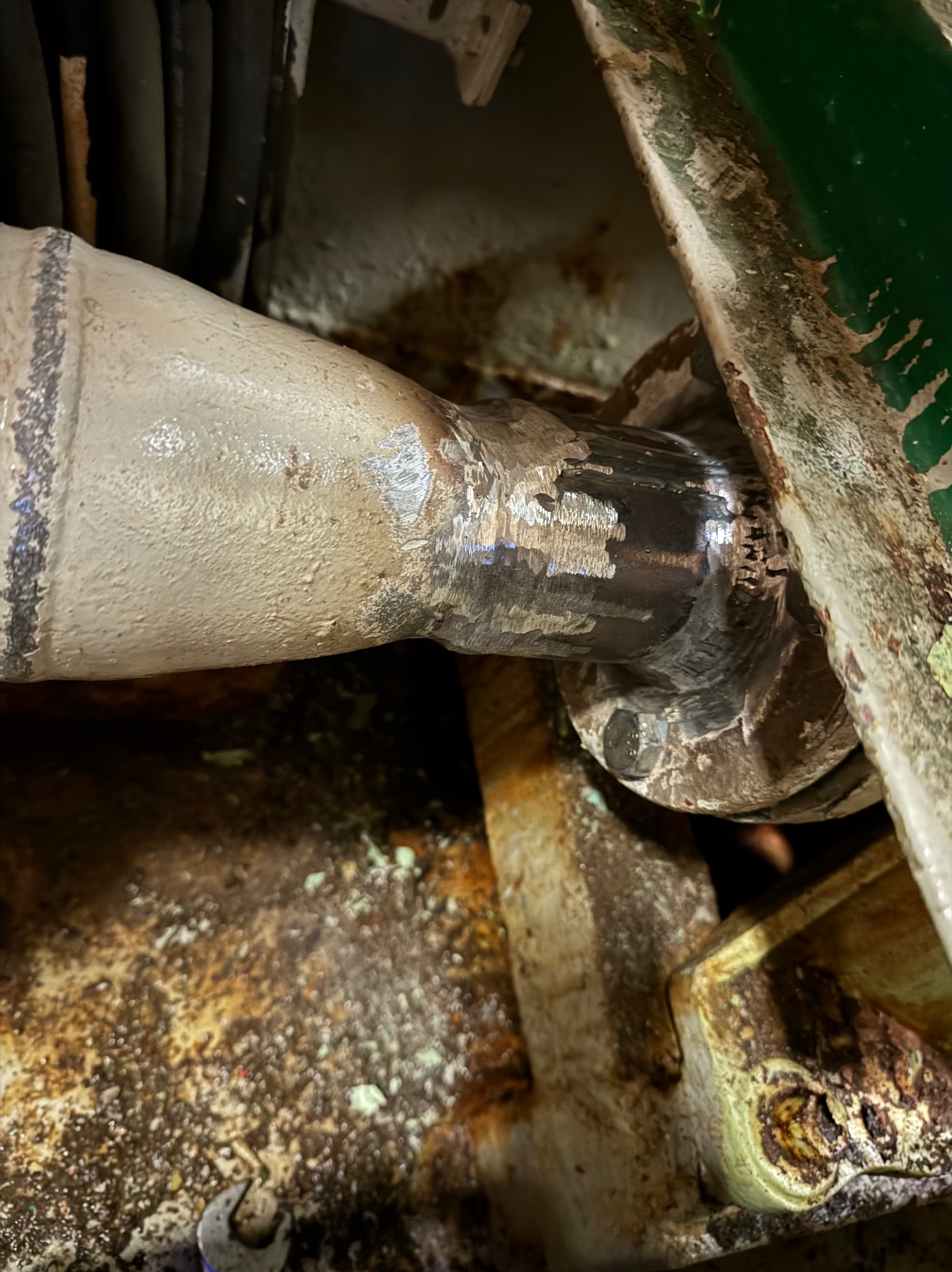 Spoina na metalowej rurze, widoczne ślady obróbki i spawania, fragment konstrukcji zardzewiałej, narzędzie w tle. Detal z bliska, surowy wygląd.