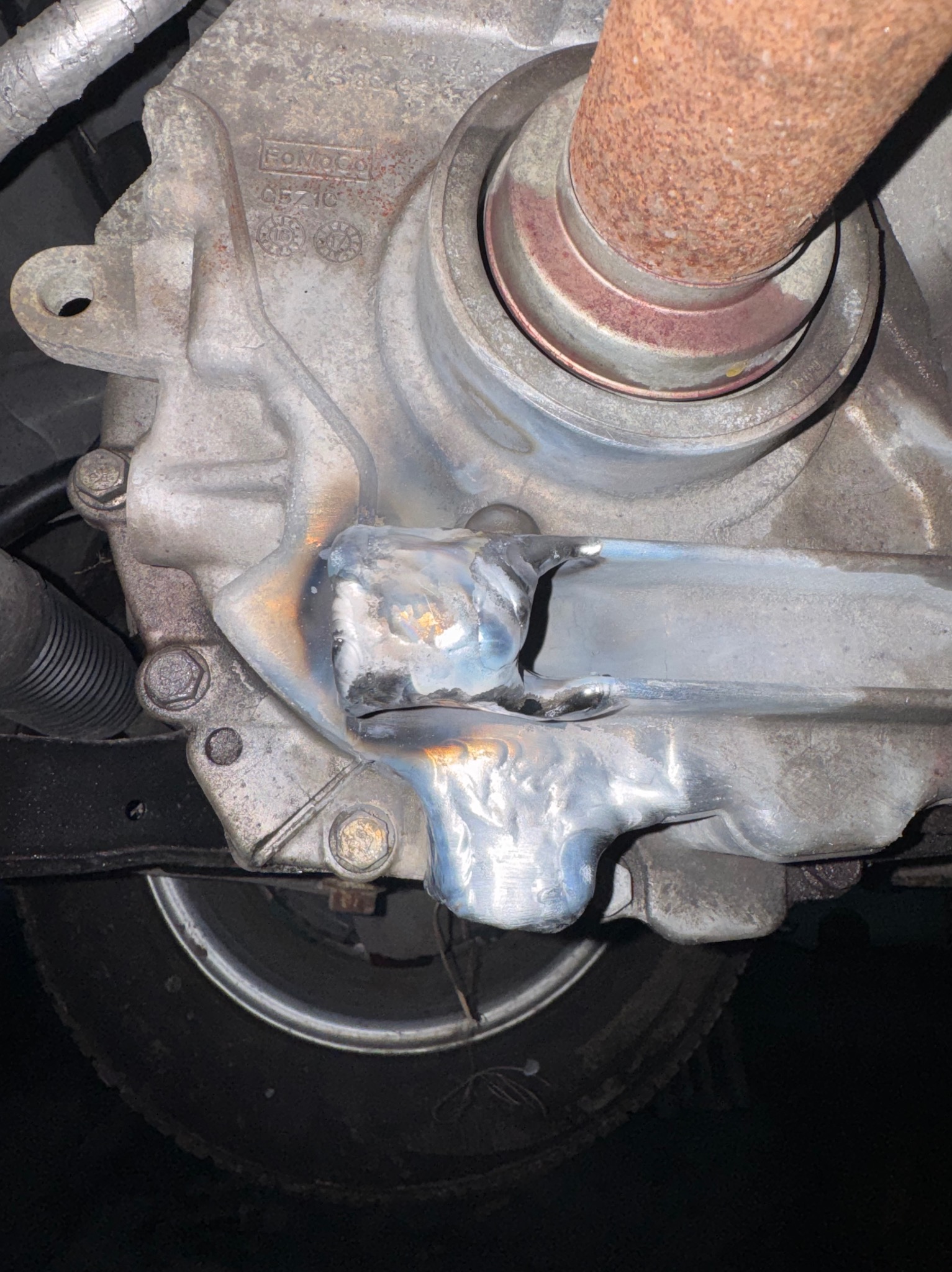 Szczegółowe ujęcie spawu na metalowej konstrukcji pojazdu, widoczne ślady obróbki termicznej i fragment opony w tle.