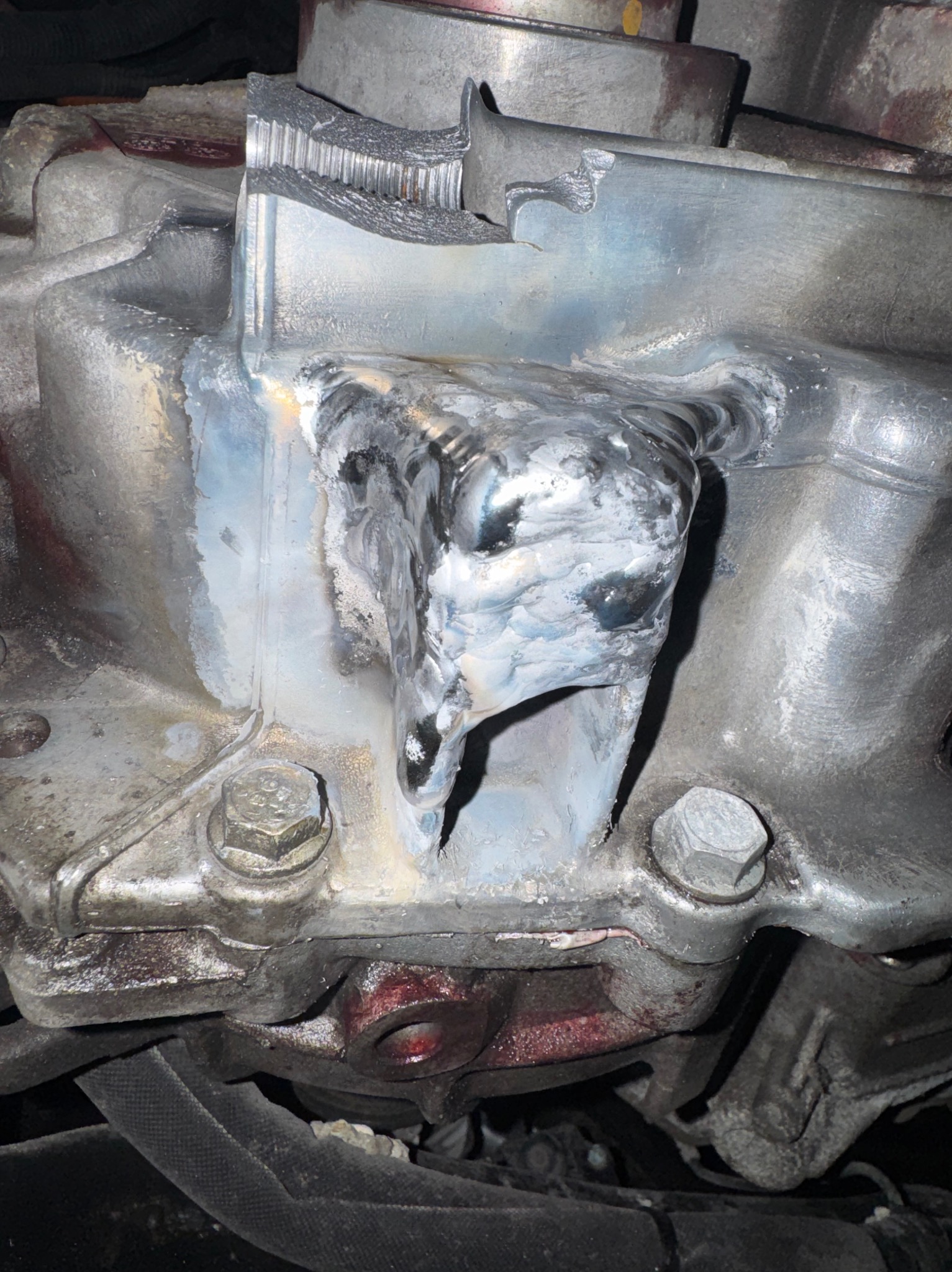 Szczegółowe ujęcie spawu na metalowej konstrukcji, widoczne ślady obróbki i mocowania śrubowe. Metal ma szary odcień z widocznymi śladami użytkowania.