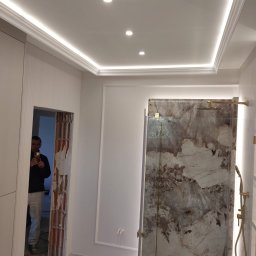 PAT House - Wykończona łazienka z kabiną prysznicową z kamienną ścianą, oświetleniem LED na suficie i pracownikiem robiącym zdjęcie w sąsiednim pomieszczeniu.