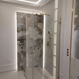 PAT House - Nowoczesna kabina prysznicowa ze złotymi detalami, marmurowym wykończeniem ścian i podświetleniem LED, widoczne przygotowane otwory na gniazdka elektryczne.