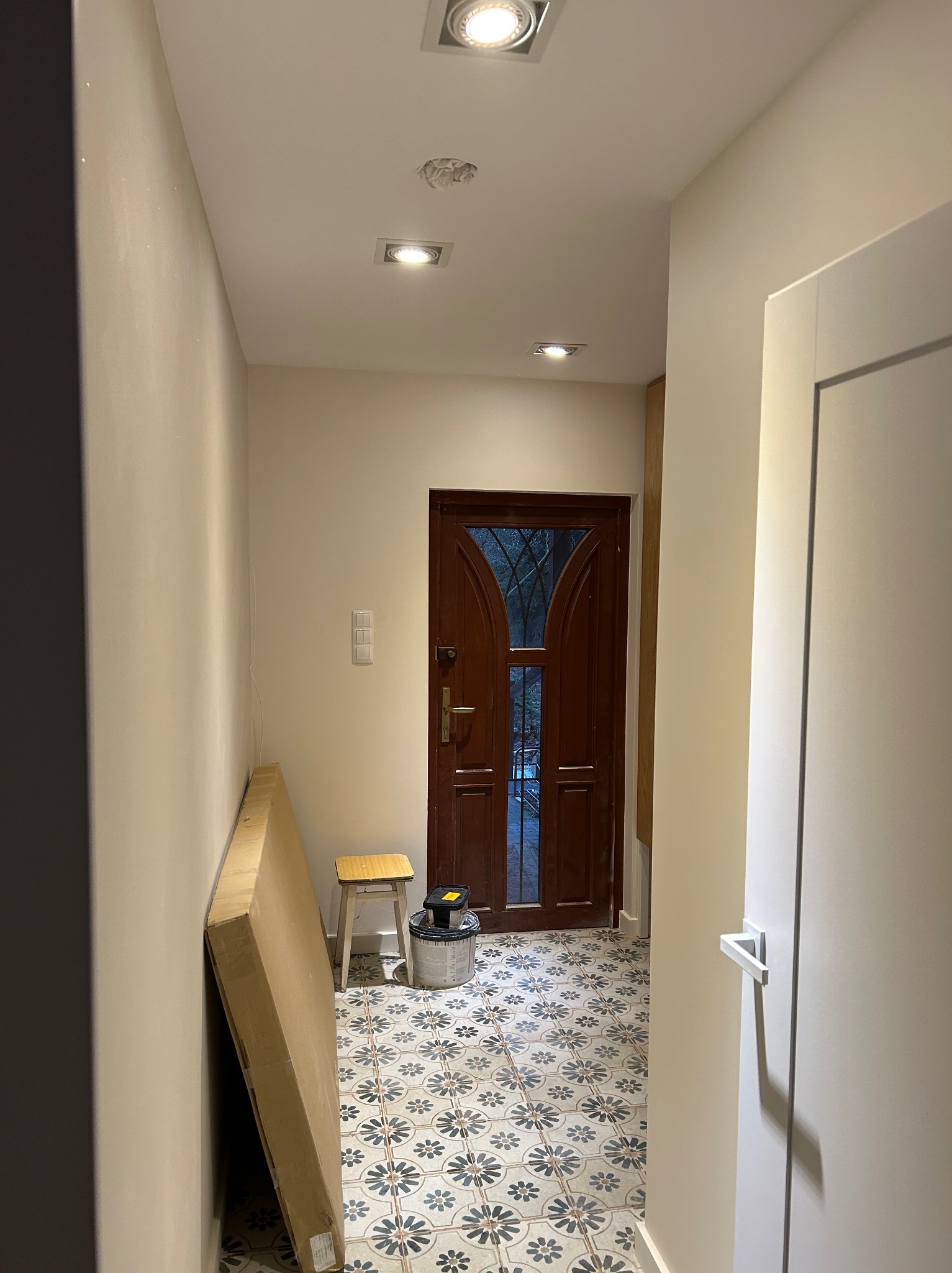 Korytarz w trakcie prac wykończeniowych: widoczna brązowa, przeszklona stolarka drzwiowa, wzorzysta podłoga, przygotowane płyty karton-gips i wiadro z farbą.