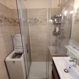 J-B.R.W Jakub Wasila - Nowoczesna łazienka z kabiną prysznicową typu walk-in, umywalką z szafką w kolorze drewna i pralką z otwartą klapą, wykończona płytkami z motywem liści.