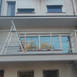 J-B.R.W Jakub Wasila - Odnowiony balkon z metalową balustradą i świeżo pomalowaną elewacją budynku. Widoczna drabina oparta o okno, sugerująca trwające prace wykończeniowe.