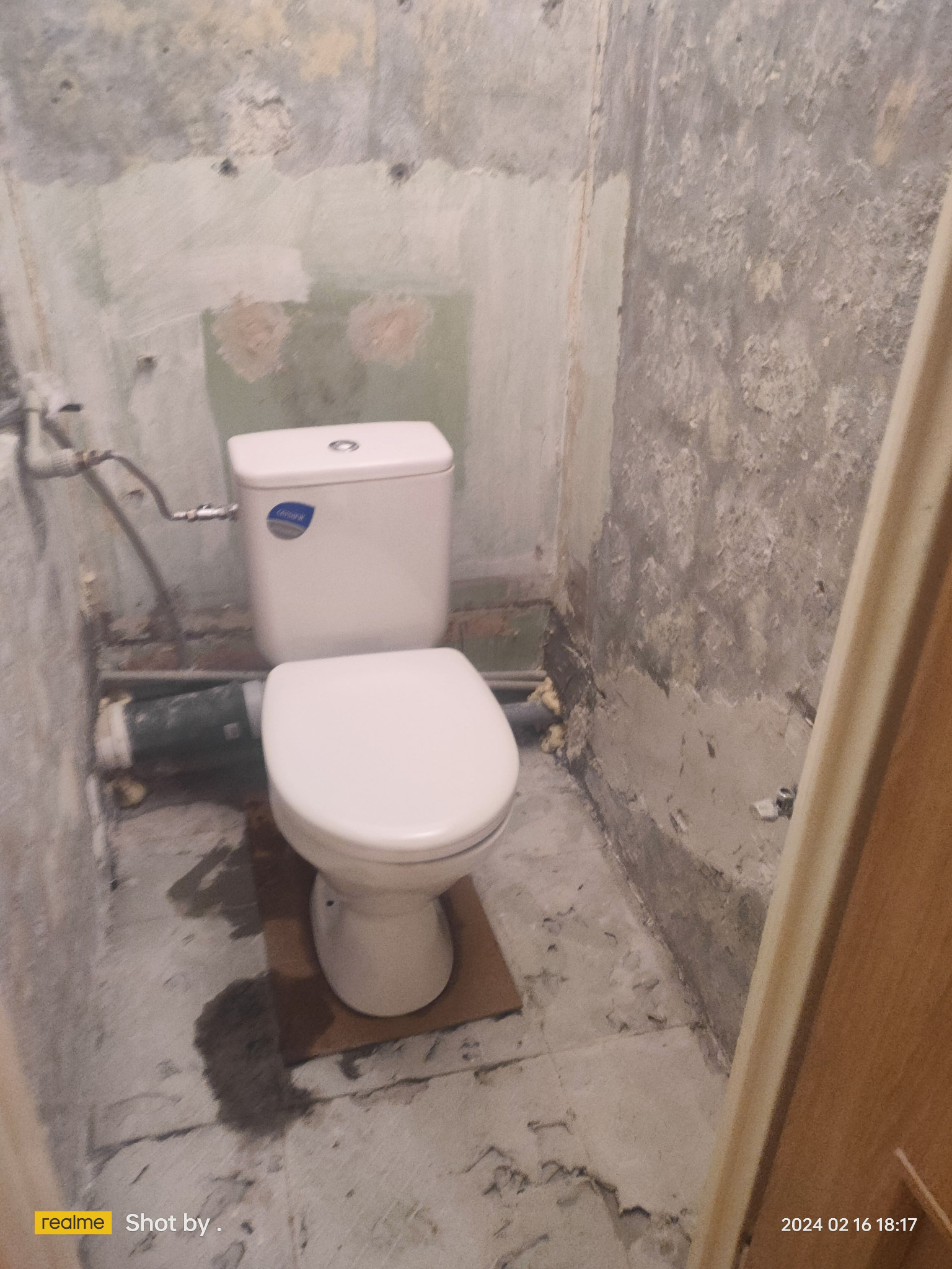 Biała toaleta w surowym stanie, ściany przygotowane do prac wykończeniowych, widoczne ślady po starych płytkach i instalacjach, podłoga z resztkami zaprawy.