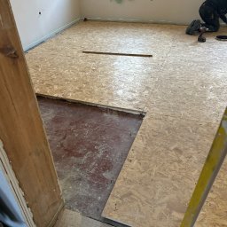 TOPAZ YEHOR TOPALOV - Układanie płyt OSB na podłodze w pokoju, widoczne narzędzia i laserowy niwelator. Część podłogi jeszcze nie pokryta płytami, widoczna stara podłoga.